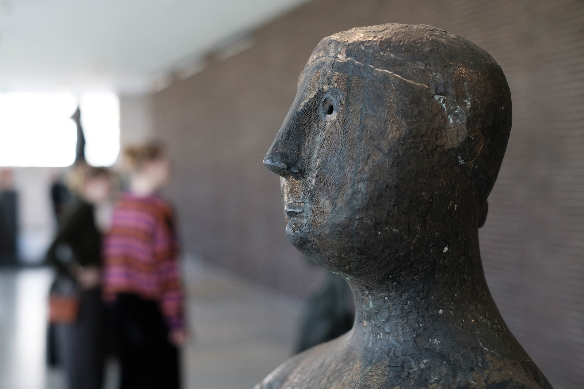 Bronzekopf einer Figur in einer Ausstellung, im Hintergrund unscharf zwei Besucher